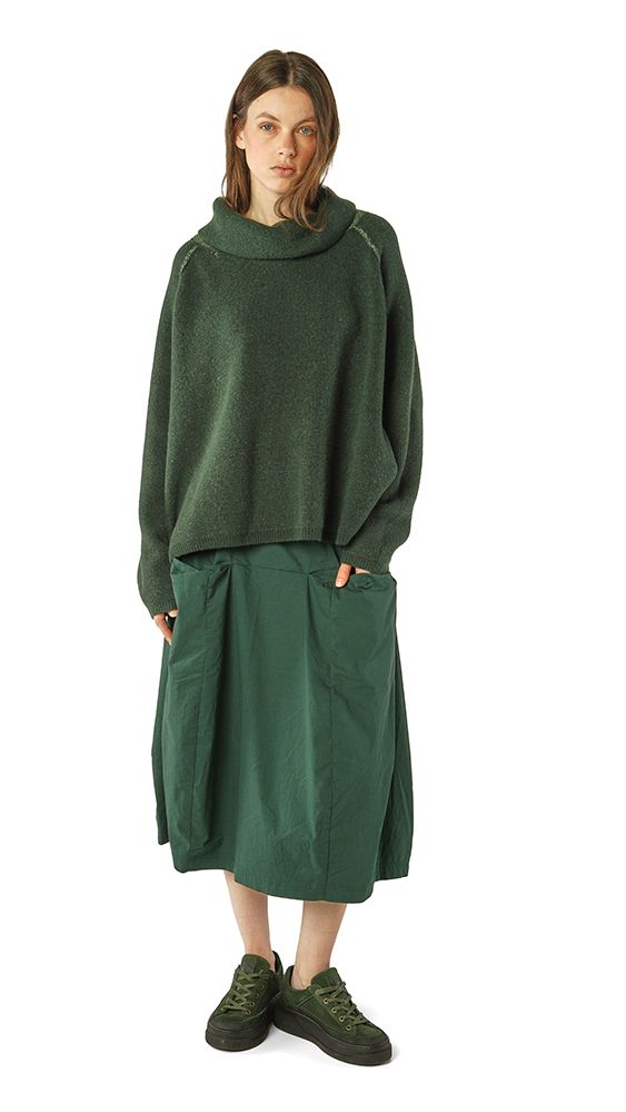 Frau trägt oversized grünen Pullover mit hochgeschlagenem Saum und grünem weitem Wickelrock, grüne Sneakers.