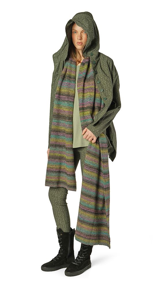 Person trägt knielangen, gemusterten Strickponcho mit Hood über grünem Top und schwarzen Stiefeln.
