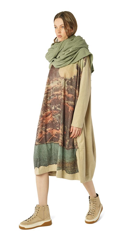 Frau trägt oversized Kleid mit Muster und Schal, beige Hosen, beige Sneakers.