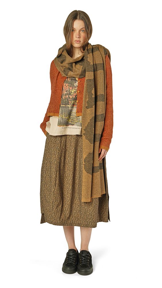 Frau trägt langes, gemustertes Kleid mit Schal und schwarzen Stiefeln, stilvoll und lässig.