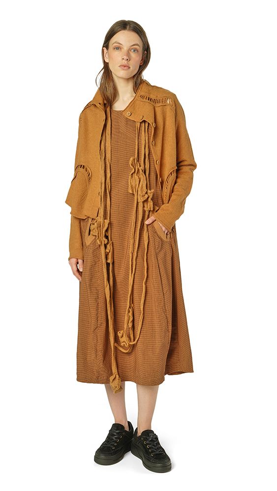Lange, beige Strickjacke mit Fransen und Kordel-Akzenten, kombiniert mit schwarzer Hose und Sneakern.