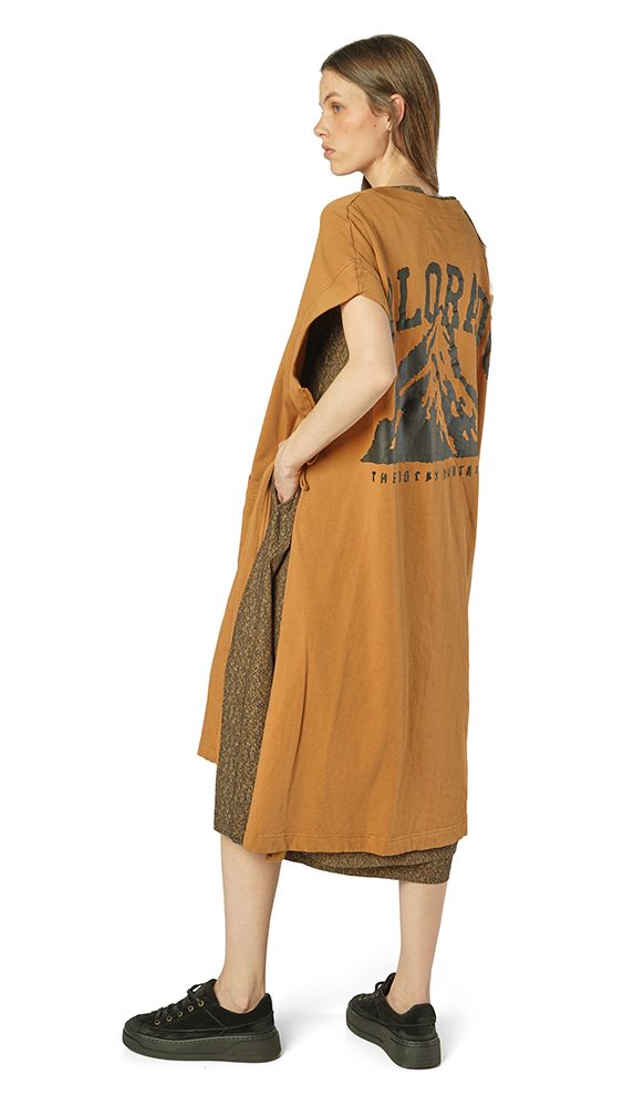 Frau trägt oversized braunes Kleid mit grafischem Druck auf dem Rücken, kombiniert mit schwarzen Sneakern.