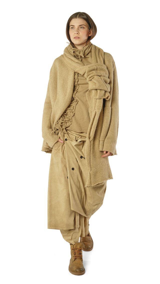 Frau trägt beigefarbenen oversized Strickmantel mit weitem Rock und Stiefeln, lässiger Look.