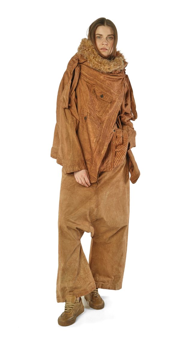 Person trägt oversized braunes Fell- und Stoff-Ensemble mit weiten Hosen und robusten Stiefeln.
