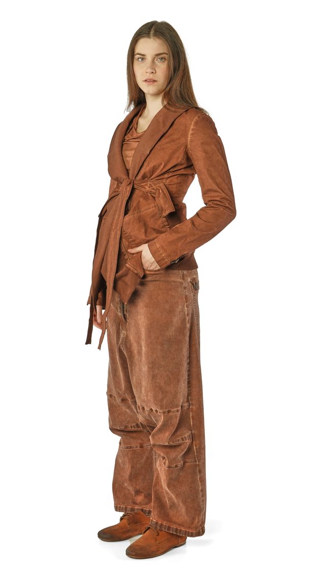 Frau trägt braunes, langes Cord-Jacket mit weitem Rock und Stiefeln, stehend.
