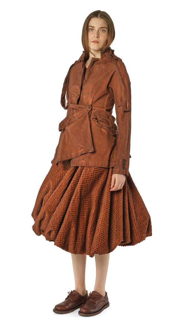 Frau trägt rustikales, braunes Wickelkleid mit weitem Rock und oversized Jacke, barfuß mit Schuhen.