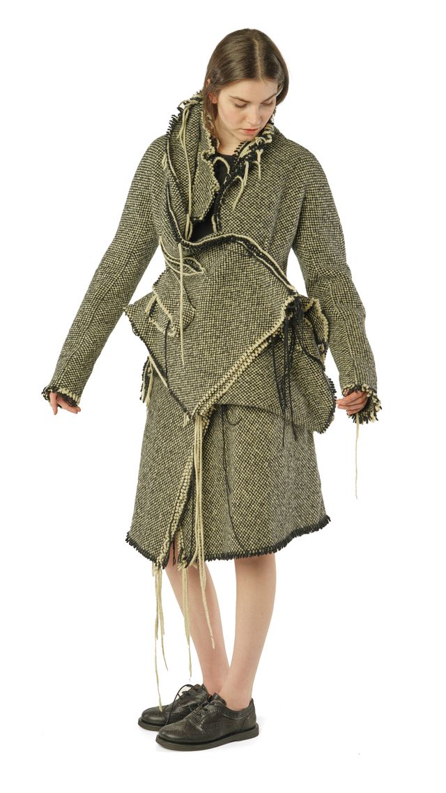 Frau trägt langes, gemustertes Trenchcoat-Kleid mit Fransen und Accessoires, schwarze Schuhe.