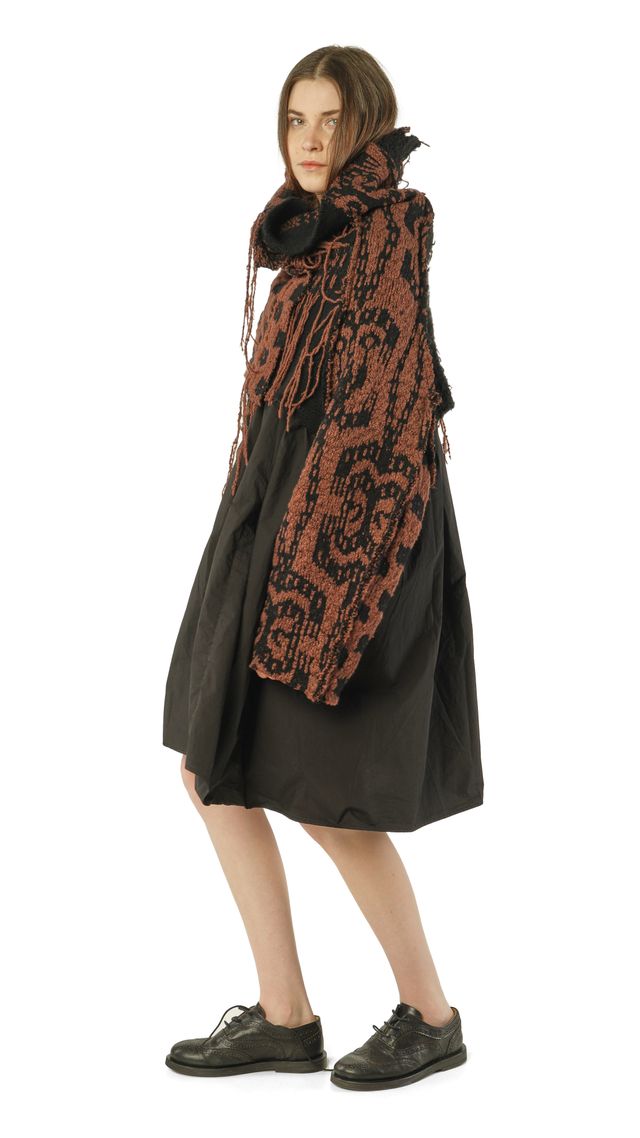 Person trägt schwarzen oversized Mantel mit orange-braunem Schal und schwarzen Stiefeln.