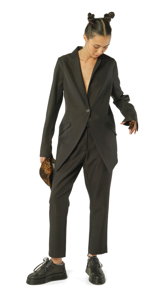 Frau in schwarzem Glitzer-Jumpsuit mit Bommel-Haartracht und Sneakern, hält Handtasche.