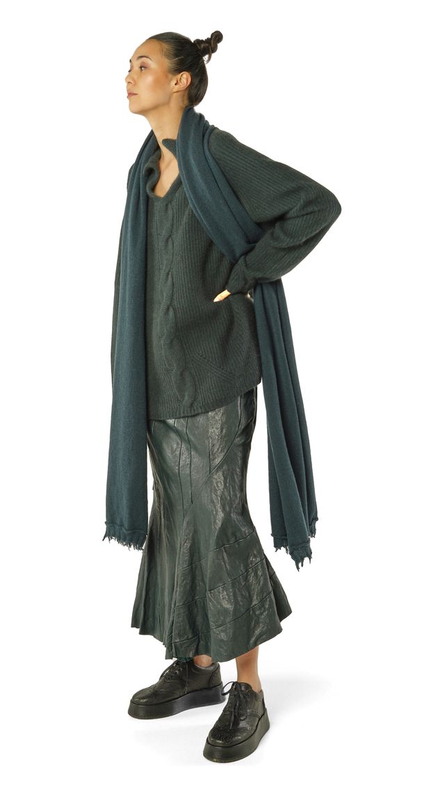 Frau trägt oversized grünen Pullover mit Schal, weitem Rock und schwarzen Sneakern.