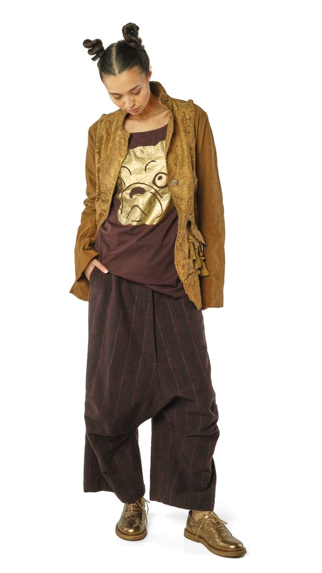 Person trägt bunte, gemusterte Kleidung mit Jacke, T-Shirt und weiten Hosen, barfuß in Schuhen.